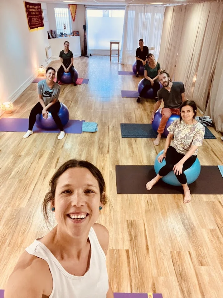 Groupe d’élèves sur des tapis dans une salle lumineuse, avec des ballons de Pilates